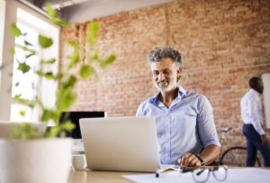 Smiling businessman using laptop in office with colleague in background